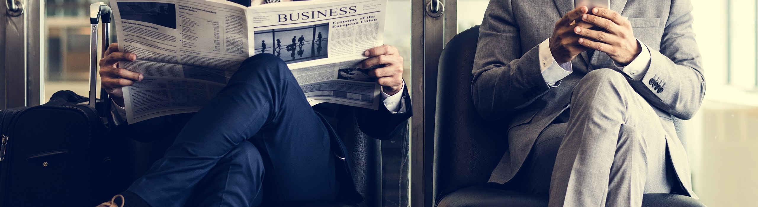 two business brokers sitting reading a business newspaper