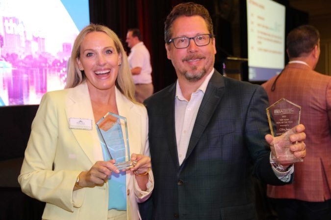 two award winners holding award and smiling