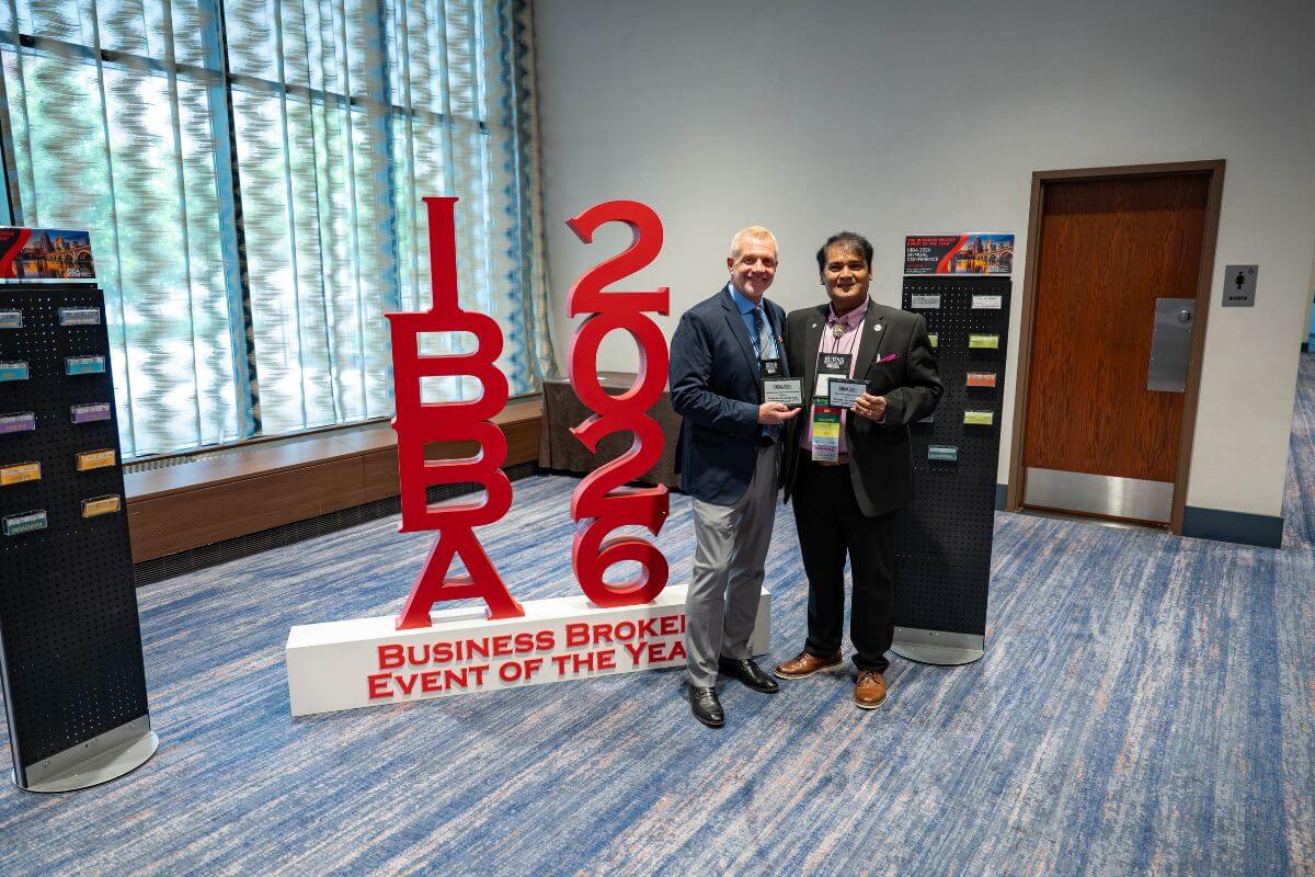 Two people pose for a picture in front of the IBBA 2026 Conference sign